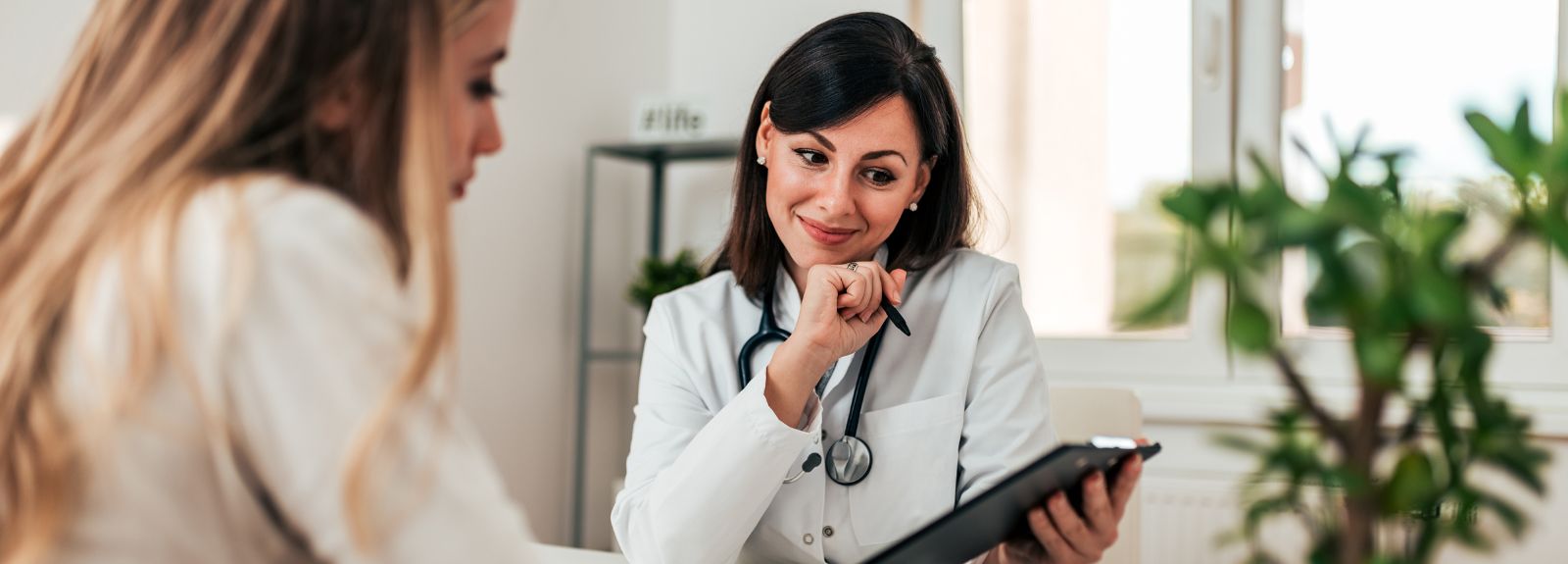 Smiling female doctor talking with another female whilst looking over information on a tablet